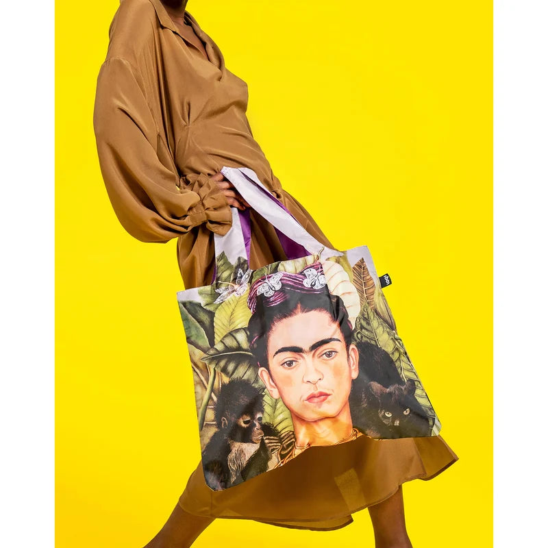 A lady's lower body swinging a Loqi shopping bag featuring Frida Kahlo on a yellow background.