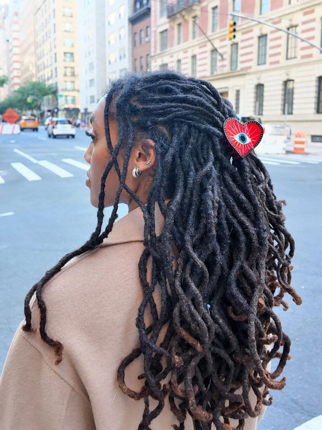 Person with long, braided hair wearing a red hair accessory on a city street.