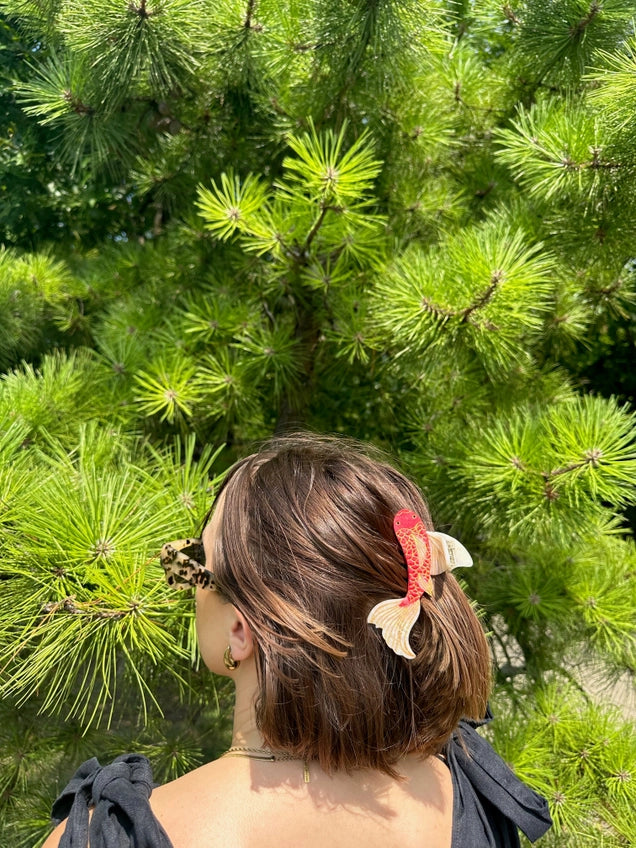 Person with decorative hair clips standing in front of a green pine tree