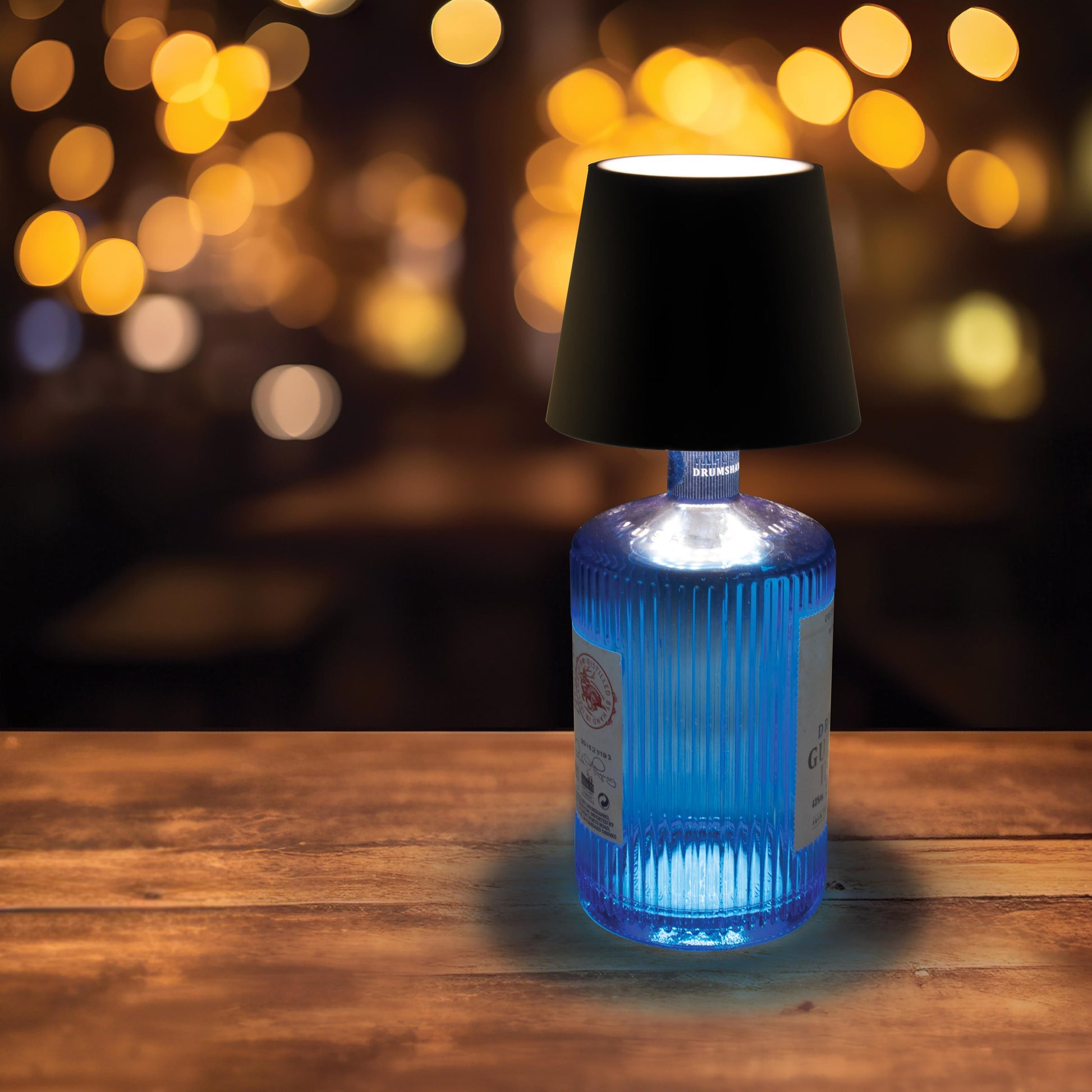 Rechargeable Bottle lamp, lit on a blue gin bottle and placed  in a nightspot setting.