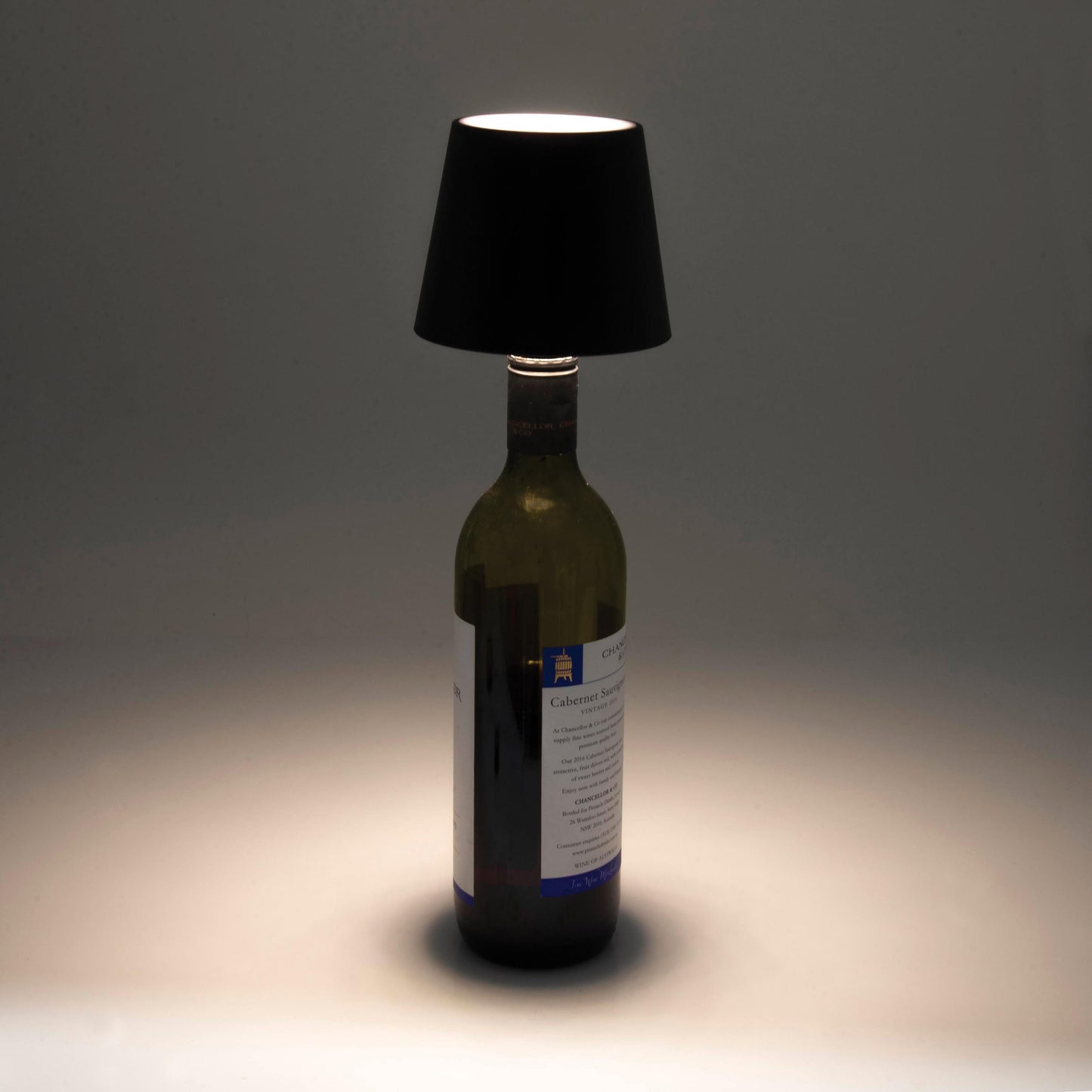 A lit  Bottle lamp on a bottle of wine placed upon a grey background.