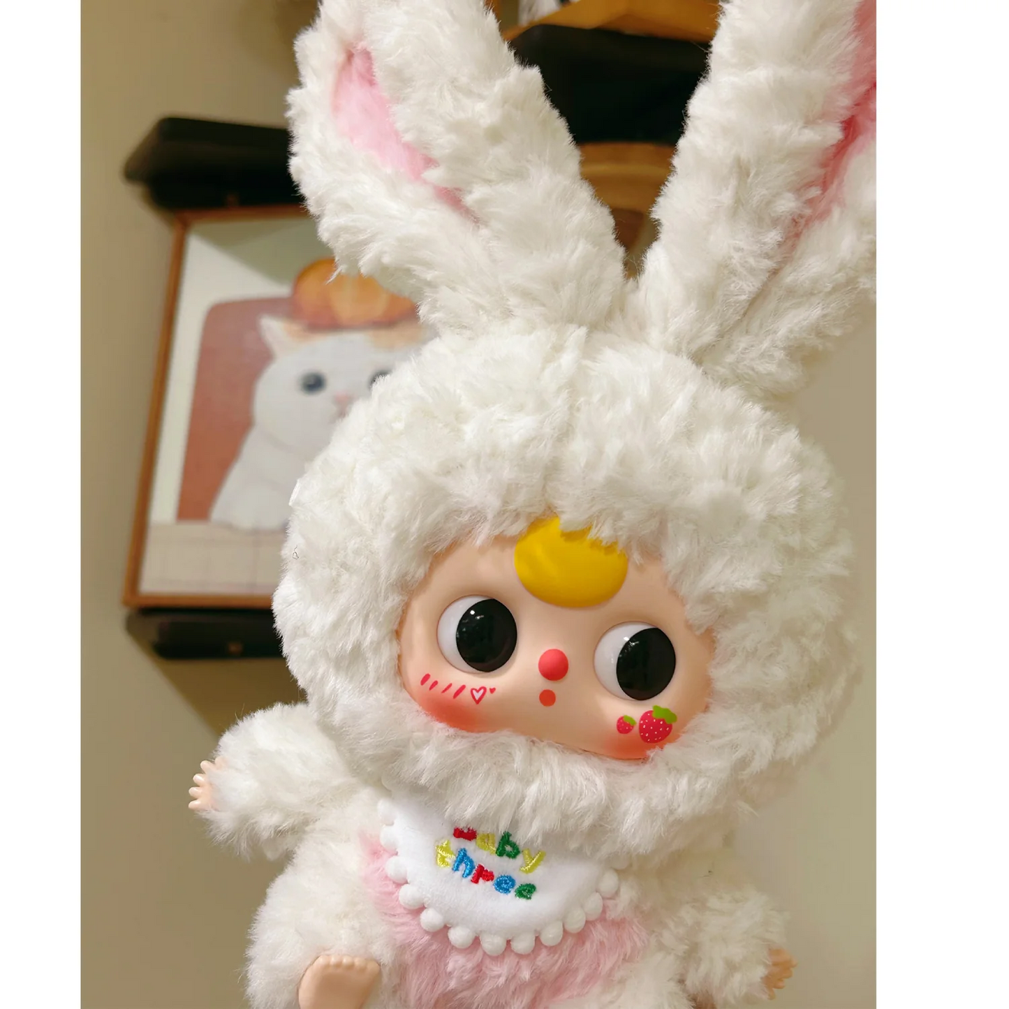 White plush toy with bunny ears and colorful face in front of a blurred background