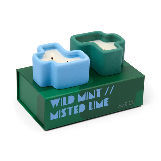 Two candles in blue and green holders on a green box labeled 'Wild Mint // Misted Lime'.