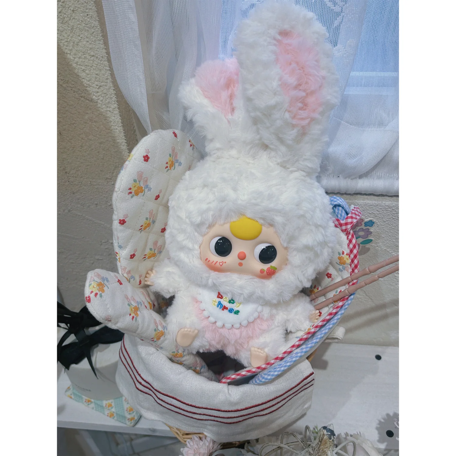 Plush toy with bunny ears and a small doll inside, sitting on a white surface.