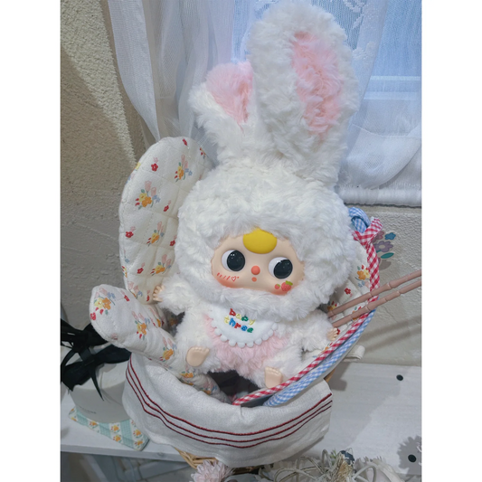 Plush toy with bunny ears and a small doll inside, sitting on a white surface.