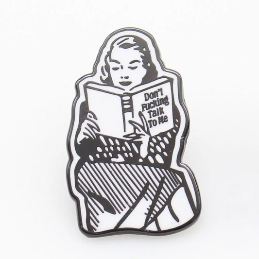 Enamel pin with a design of a person reading a book titled 'Don't Fucking Talk to Me' on a white background.