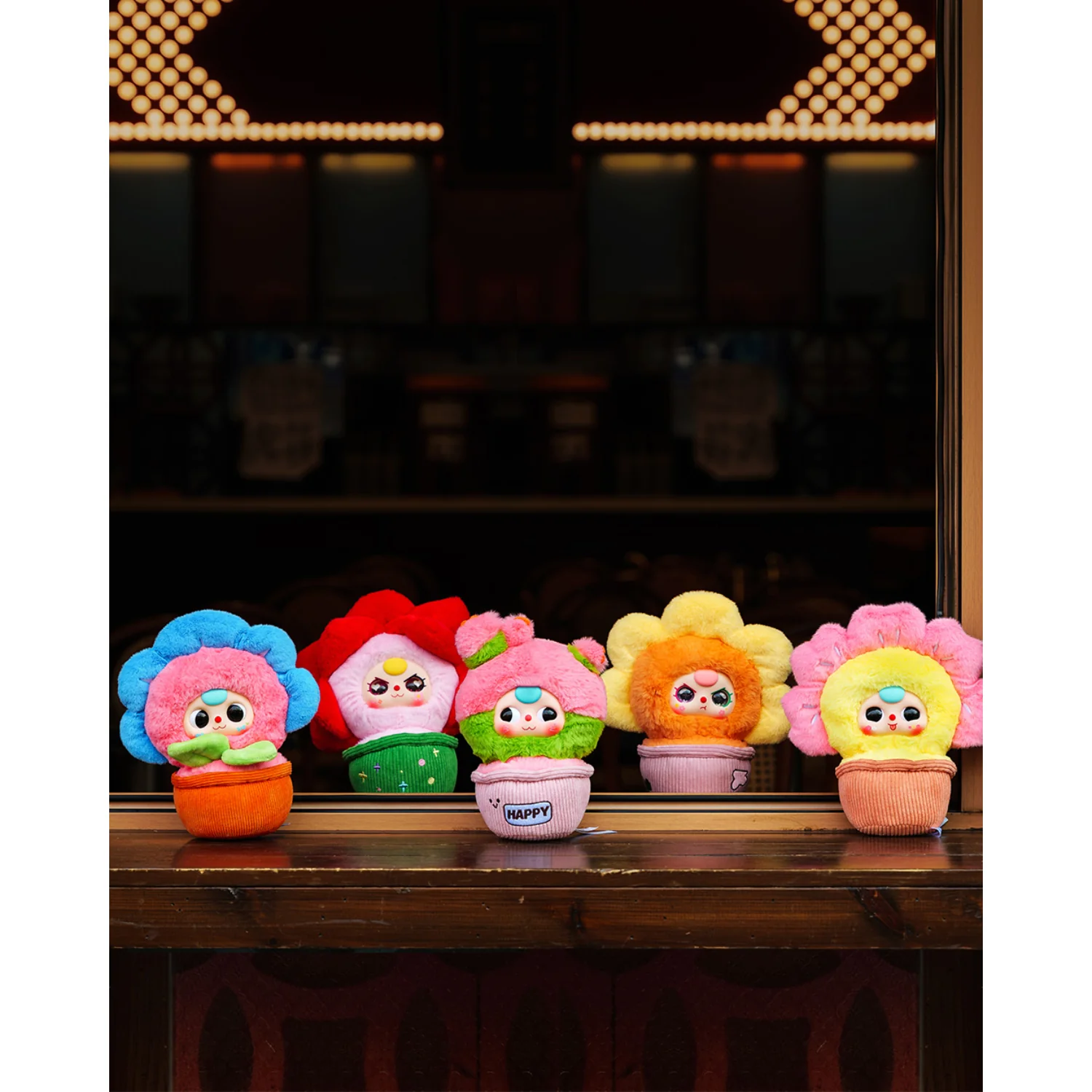 Five colorful plush toys resembling flowers with faces on a wooden surface.