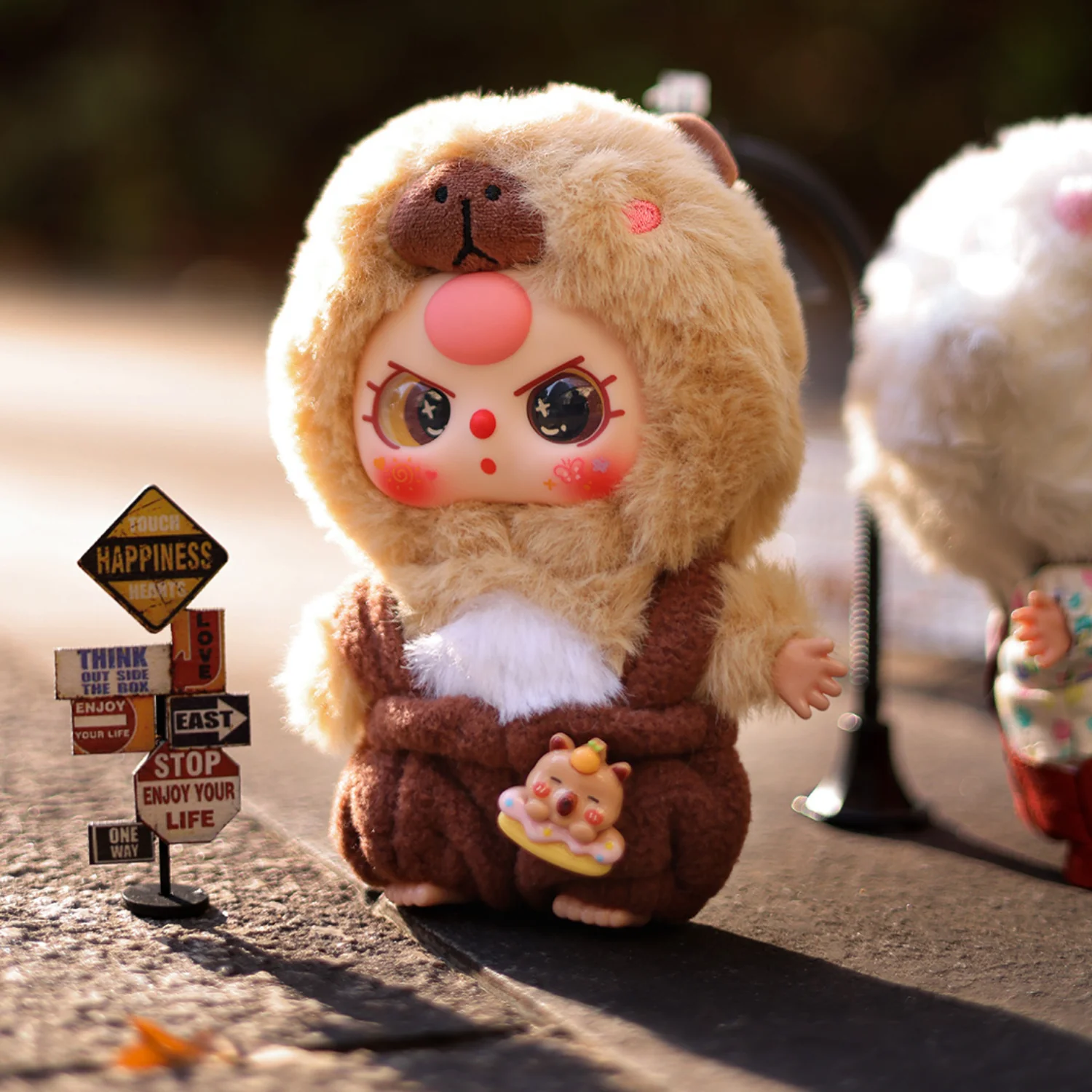 Plush toy resembling a bear with a face, sitting outdoors on a sunny day.