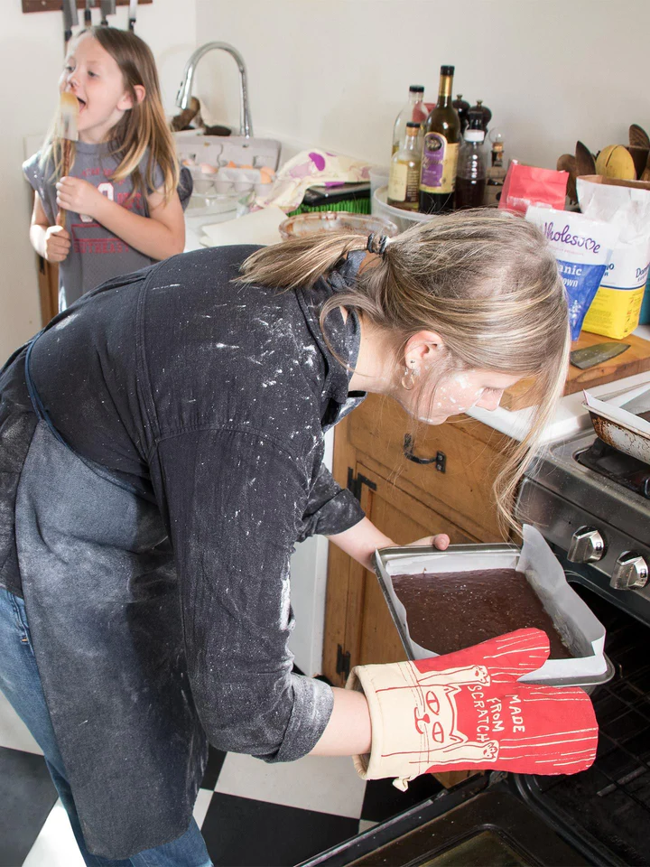 Woman taking a tray of brownies out of an oven with a child in the background.
