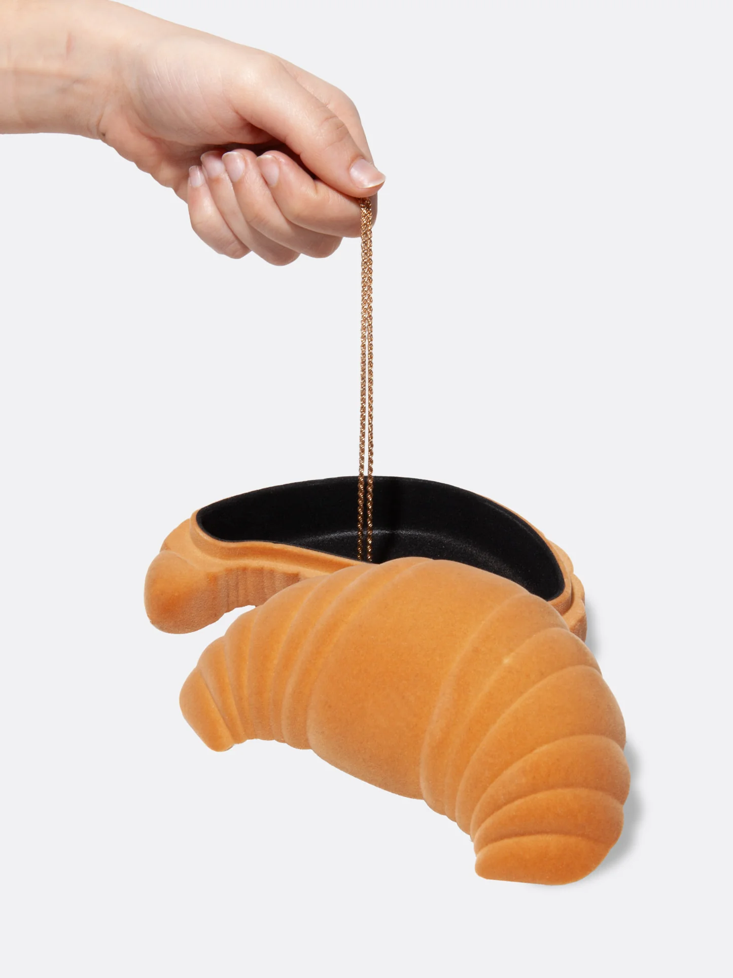 Hand holding a croissant-shaped object with a black interior on a light gray background