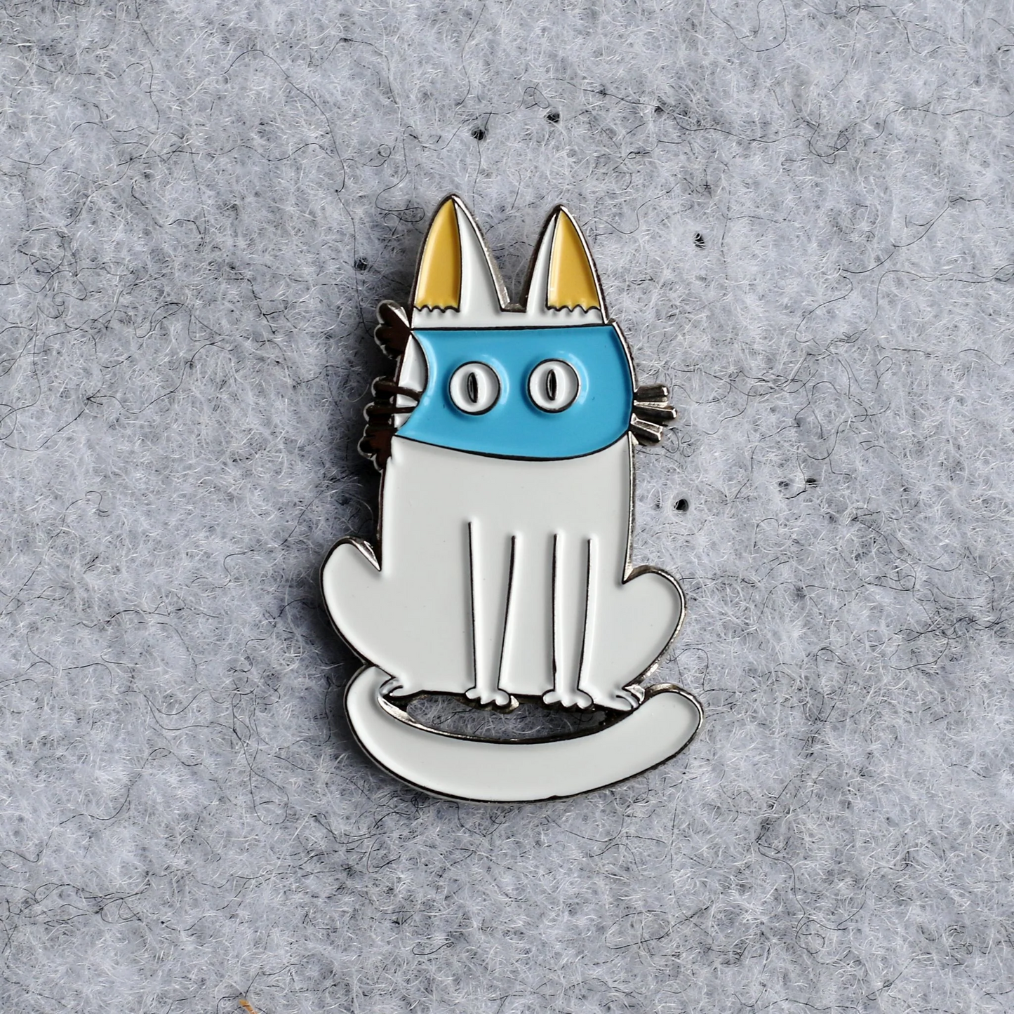 Cat-shaped pin with blue face and yellow ears on a gray textured background