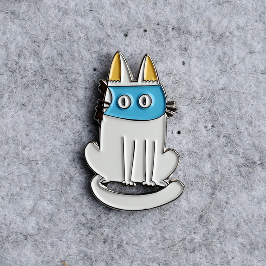 Cat-shaped pin with blue face and yellow ears on a gray textured background