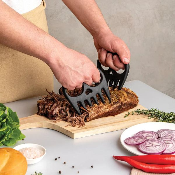 A person's hands shredding some meat using the meat munchers on a bench.