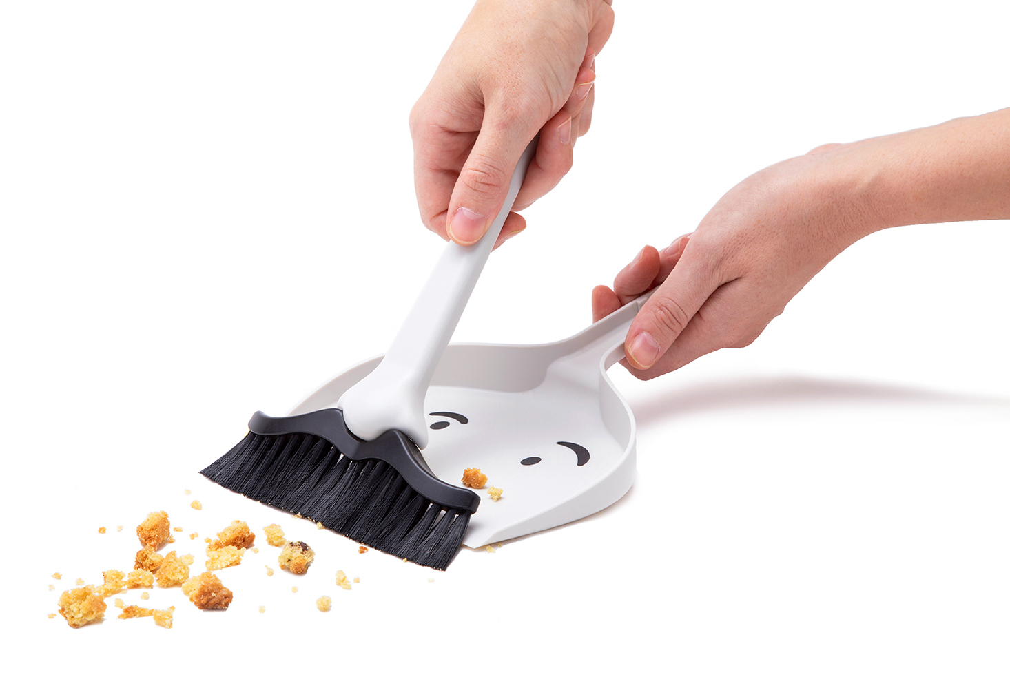 Two hands sweeping up baking crumbs from a white surface.