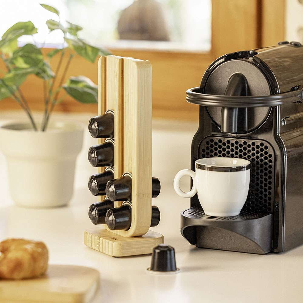 Coffee machine with a white cup and wooden capsule holder on a kitchen counter.