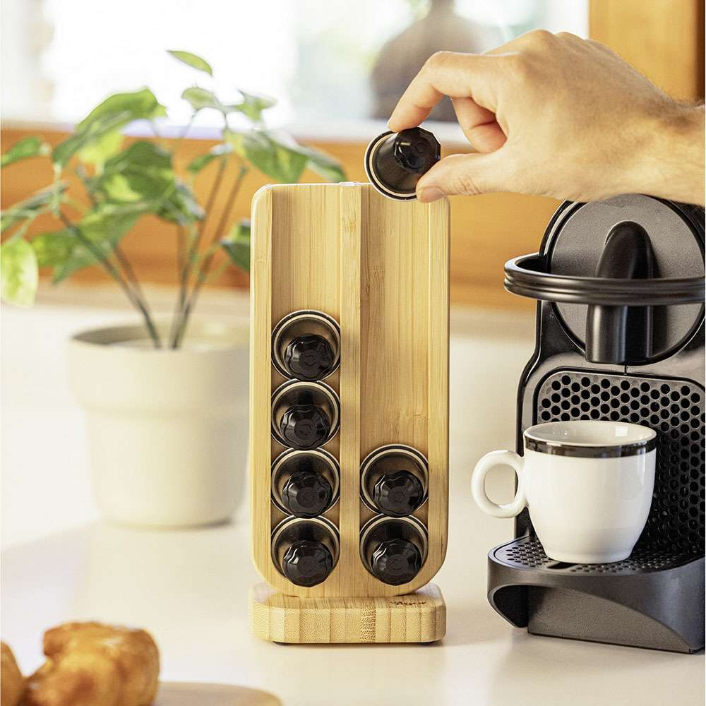 Wooden coffee pod holder with coffee pods next to a coffee machine on a kitchen counter.