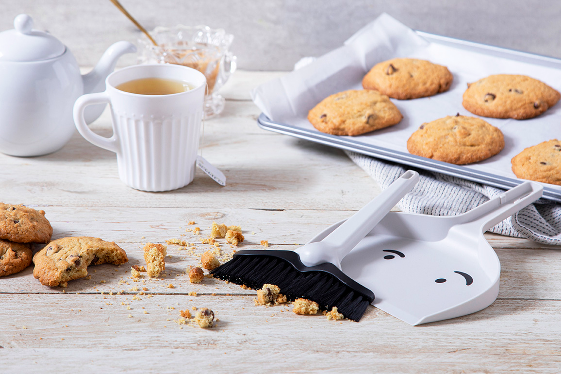 A cup of tea and a tray of cookies. The Dustache dustpan in the foreground is picking up the cookies crumbs.