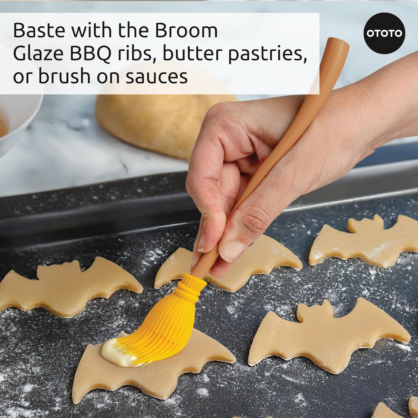 A hand basting some bat shaped cookies with the yellow pastry brush.