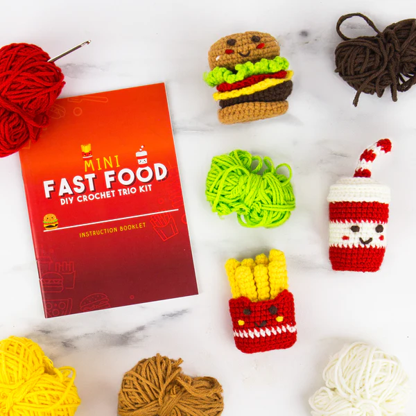 Miniature crocheted fast food items with an instruction booklet on a marble surface.