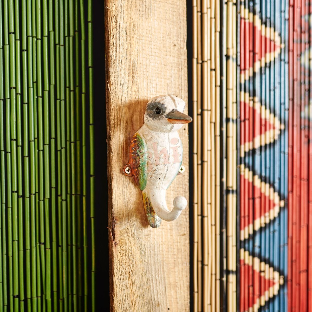 Decorative bird-shaped hook on a wooden surface with a colorful geometric pattern in the background.