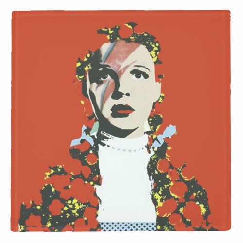 A square glass coaster featuring a pop-art portrait of Judy Garland and Starman with red, white, black, and yellow floral elements on a solid red-orange background.