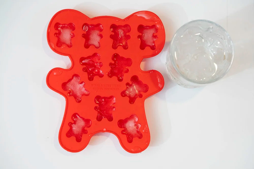 Red bear-shaped ice cube tray with a clear glass on a white background
