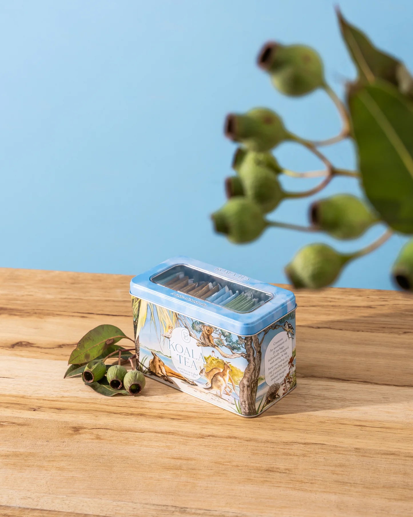 Decorative container with nature-themed design on a wooden surface with greenery in the background