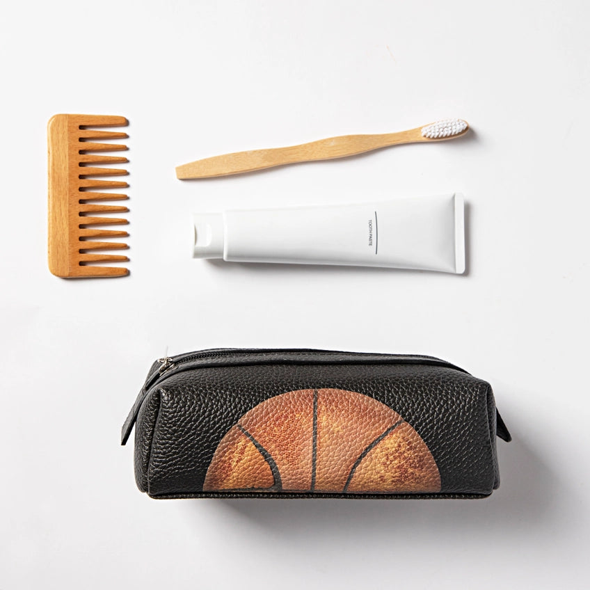Black toiletry bag with basketball design, wooden comb, toothbrush, and white tube on a light gray background
