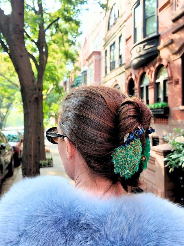 Person with styled hair and peacock hair claw and blue fur coat on a city street
