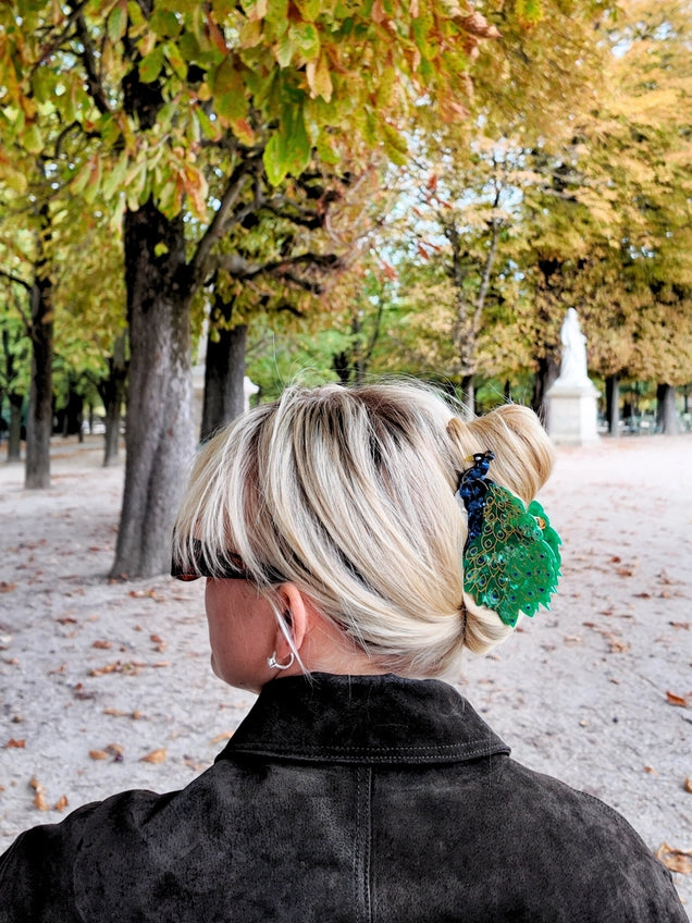 Person with styled hair and peacock hair clip in an outdoor setting with trees 