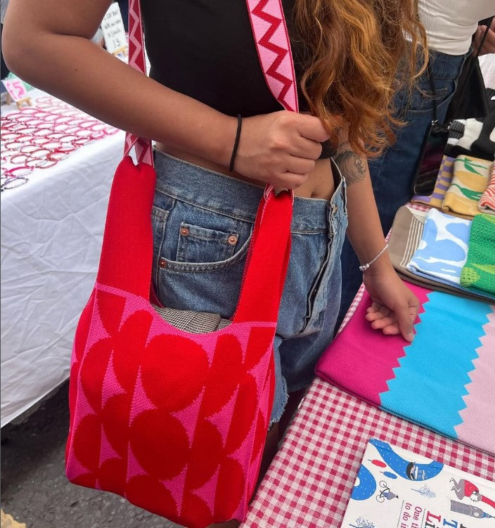 red geometric bag held by female leaning against a table.