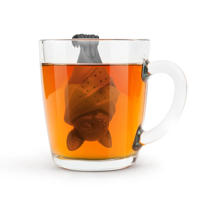 A black bat tea infuser steeping in  tea  in a  glass mug on a white background.