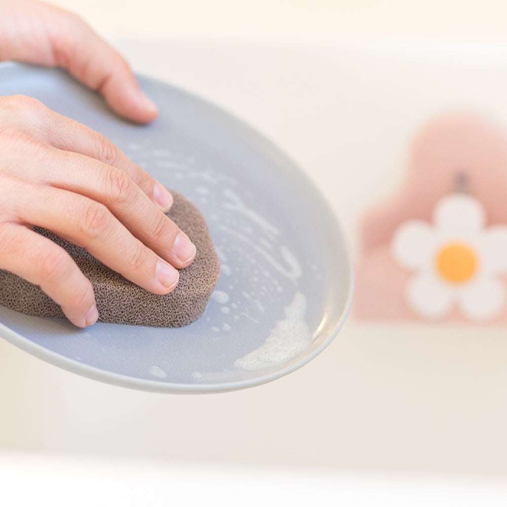 Person cleaning a ceramic plate with a sponge on a light background