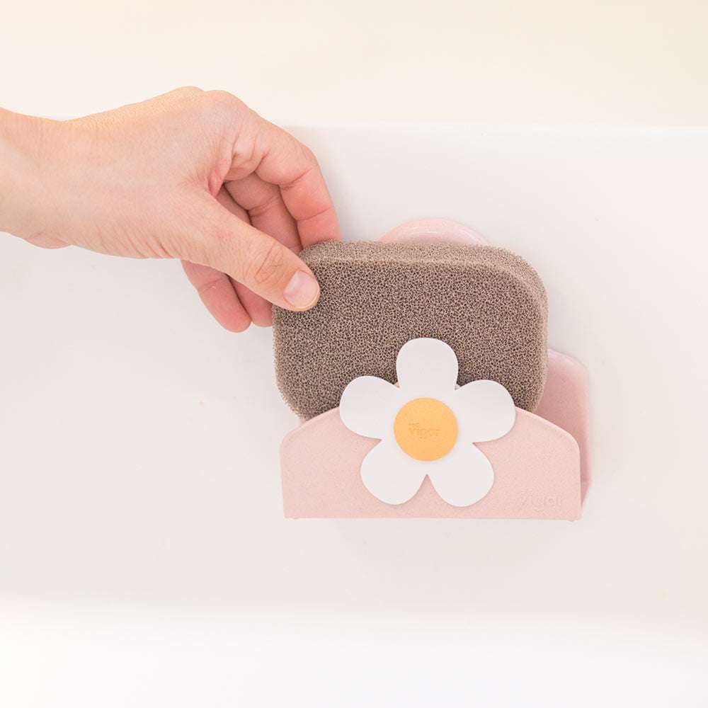 Small brown sponge and pink rectangular container with a white flower design on a light background