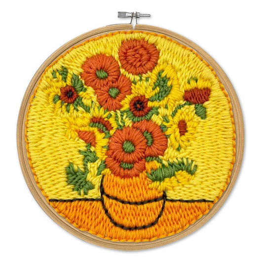A circular wooden embroidery hoop containing a colorful floral tapestry or embroidered design of sunflowers in a vase, shown against a plain white background.