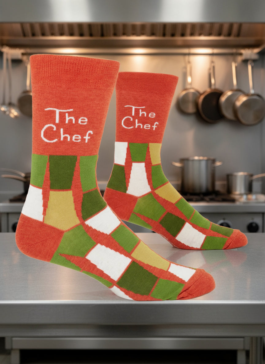 An orange and green patterned pair of BLUE Q "The Chef" men's crew socks  on with a commercial kitchen background|Gizmo Gifts