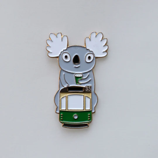 Pin with a koala holding a cup on a tram against a light gray background