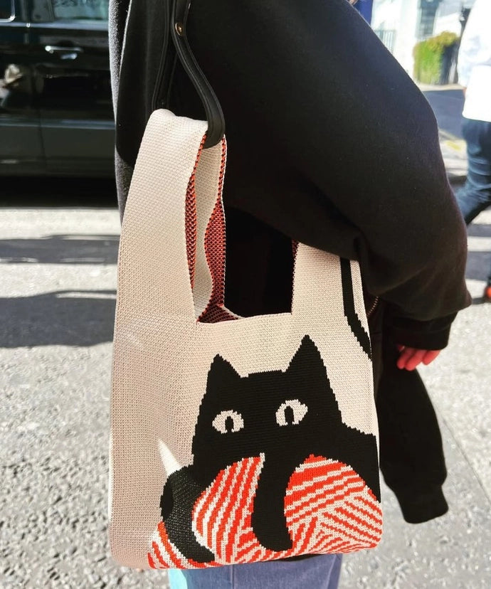 Person holding a tote bag with a cat design outdoors