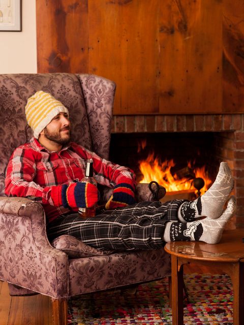 A man reclining on a chair in front of a fire place wearing BlueQ-Men's crew socks "Worst gift ever"